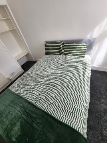 a bed with a green and white blanket and a pillow at The Maple in Grays Thurrock