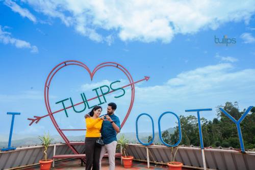 a man and woman standing in front of a heart sign at Tulips Resorts - Village in Ooty