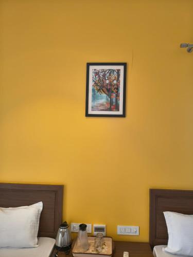 a yellow wall with a picture above two beds at Abhushan Mahal in Nīmri