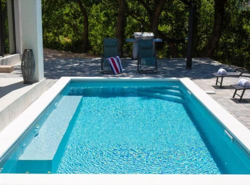 a blue swimming pool with two chairs and a table at Wellness villa Modruna in Grižane