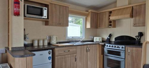 a kitchen with wooden cabinets and a microwave at Superb 8 Berth Dog Friendly Caravan To Hire In Norfolk Ref 10054B in Belton