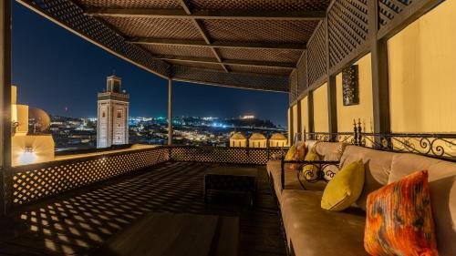 a balcony with a couch and a clock tower at night at Riad Dar Pierre in Fès