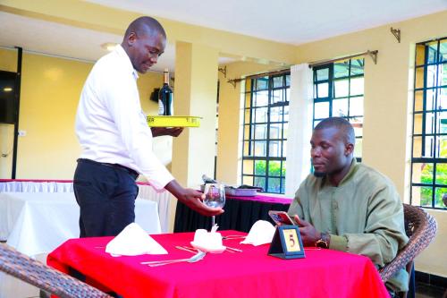 a man pouring a man a glass of wine at a table at Divine Homes Resort Kisumu in Kisumu