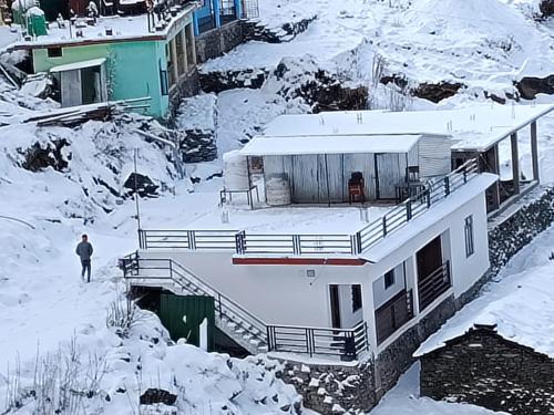 a house in the snow with a man walking past it at Jaggi Guest House Chopta in Chopta