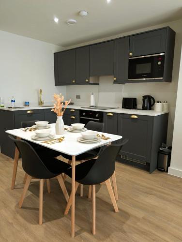 a kitchen with black cabinets and a white table and chairs at Leeds Arena Luxury Appt in Leeds