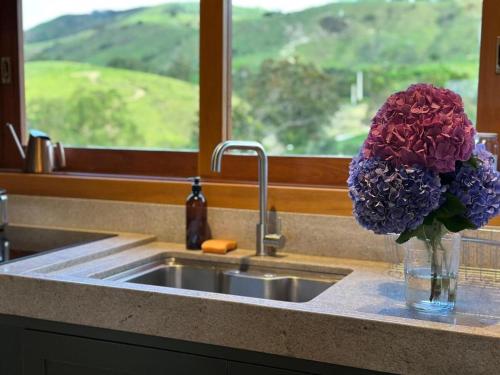 a vase of purple flowers sitting next to a sink at Casa de Campo - Quintal Infinito in São Luiz do Paraitinga