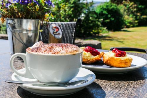 a cup of coffee sitting on a table with two pastries at The Bay Rooms at Glenisle Hotel in Lamlash