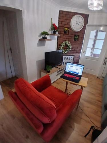 a living room with a red couch and a laptop on a table at Rose Cottage-4 BED HOUSE FOR CONTRACTORS & FAMILIES Close to M6, J10-NO PARTIES ALLOWED in Walsall