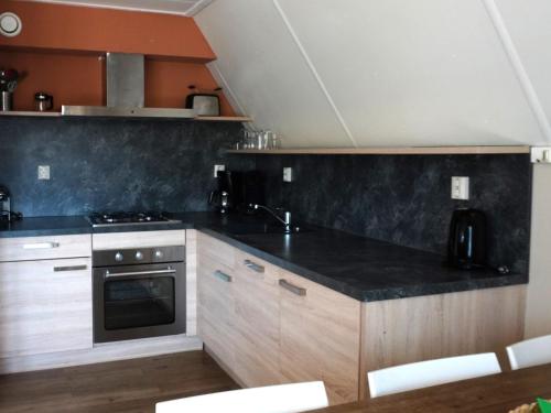 a kitchen with wooden cabinets and a black counter top at Holiday Home Ruiten AA comfort by Interhome in Vlagtwedde