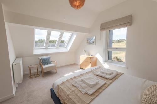 a white bedroom with a bed and two windows at Tai Porth Llechog Bungalow By Birch Stays in Amlwch