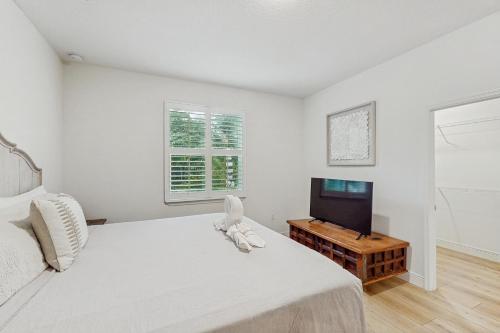 a white bedroom with a bed and a flat screen tv at Captain's Quarter in Sebastian