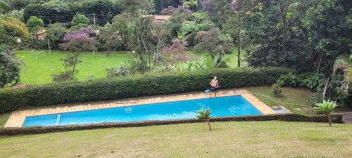 a woman is standing next to a swimming pool at Recanto da Morgana-Lofts bem equipados, conforto e piscina grande in Teresópolis