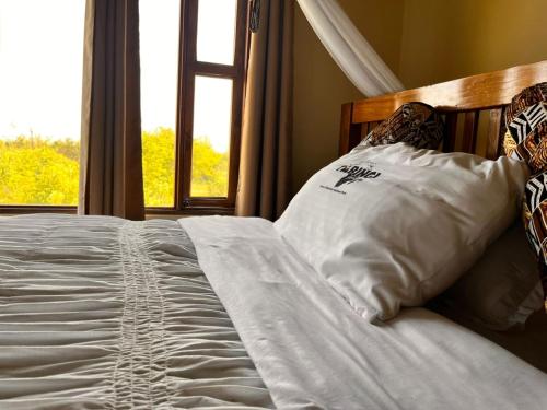 a bed with white sheets and pillows with a window at Tabingi Safari Lodge in Katunguru