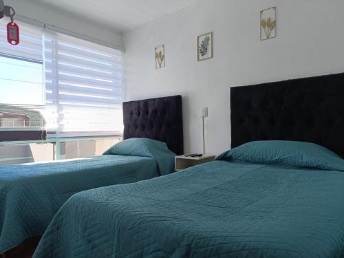 two beds in a bedroom with green sheets and a window at Hotel del centro rancagua in Rancagua