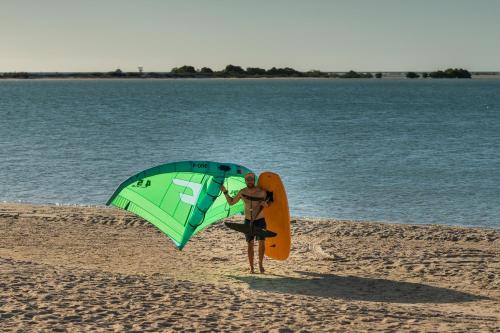 a man standing on the beach with an umbrella and a surfboard at Soledade Bangalôs - Kauli Seadi in Macau