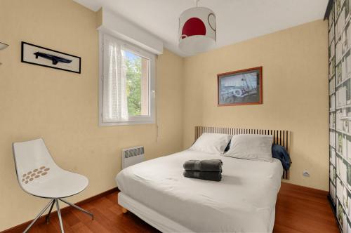 a bedroom with a white bed and a white chair at Le Jardin des Muses - T3 climatisé avec terrasse, Piscine et Parking in Toulouse