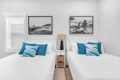 two beds in a white room with blue pillows at Luxury 5BR- Heated Pool FREE for Sept-Oct in Carolina Beach