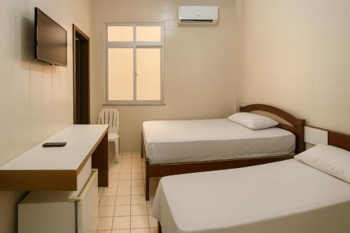 a small room with two beds and a desk at Hotel Lídia in Fortaleza