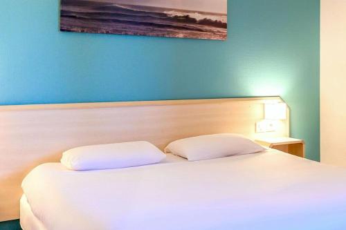 a bedroom with a white bed with a blue wall at Comfort Hotel Orleans Saran in Saran