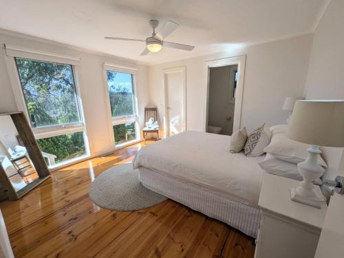 ein weißes Schlafzimmer mit einem Bett und zwei Fenstern in der Unterkunft Kookaburra Cottage- views, wineries, sanctuary, in Healesville