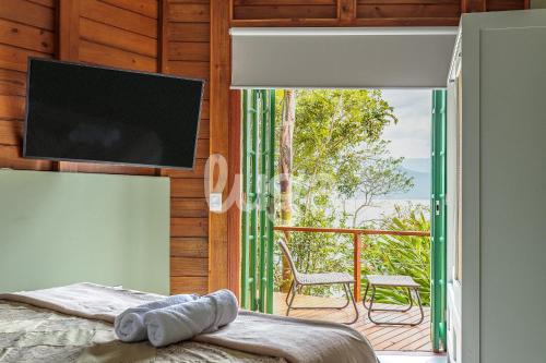 a bedroom with a bed and a balcony with a television at Refúgio pé na areia na Caieira - Espaço completo in Florianópolis