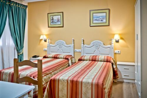 two beds in a hotel room with green curtains at Hostal Carmen in Zafra