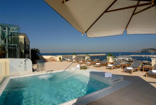 una piscina con sedie e ombrellone su un patio di Hotel Villa Carolina a Ischia