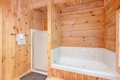 a bathroom with a tub and wooden walls at Lazy Dog Log Cabin, Hot Tub, Fishing Lake, New River Access, Foosball in Wagoner
