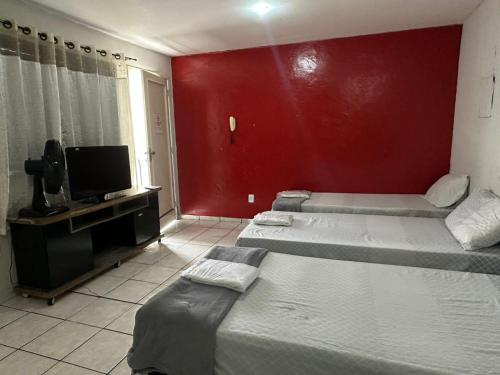 two beds in a room with a red wall at Hotel Paradão Linhares in Linhares