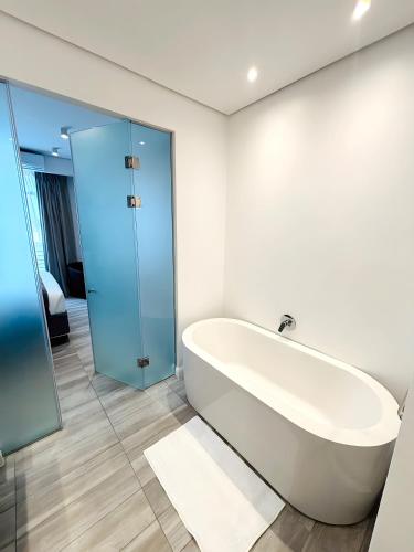 a white bathroom with a tub and a glass door at Menlyn Maine Residences in Pretoria