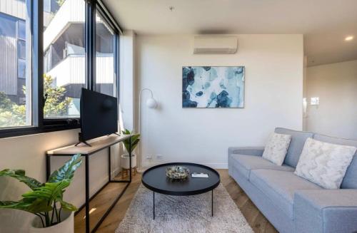 a living room with a blue couch and a table at Chic Cosy 2BR Retreat with Rooftop Spa BBQ in Melbourne