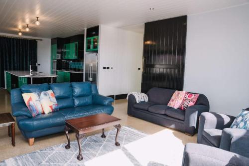 a living room with blue couches and a kitchen at Saltwood Peterborough in Peterborough