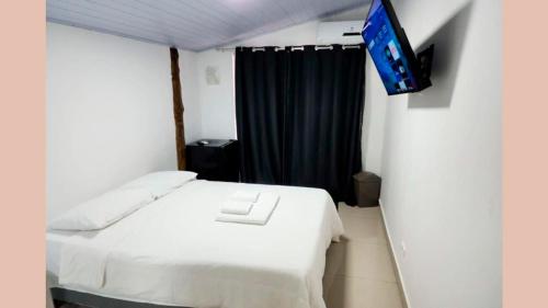 a bedroom with a white bed and a flat screen tv at Maresias Suítes in Maresias