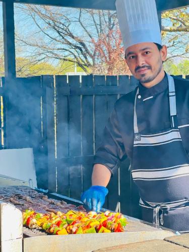 a man in a chef hat preparing food on a grill at Distinction Heritage Gateway Hotel in Omarama