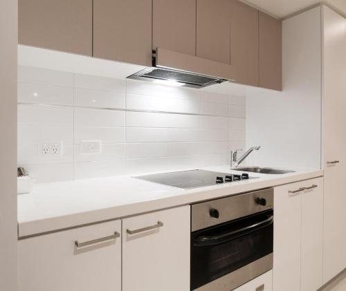 a white kitchen with a sink and a stove at Oaks Adelaide Horizons Suites in Adelaide
