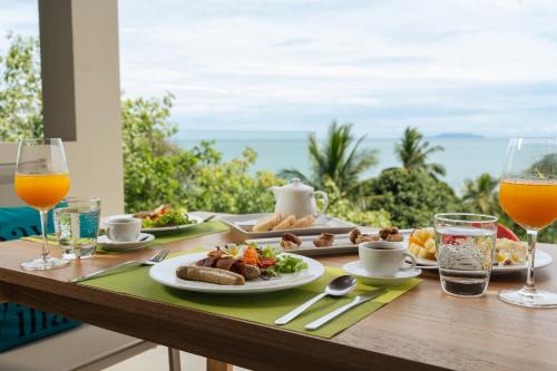 a table with plates of food and glasses of orange juice at Bay Villas Koh Phangan in Salad Beach