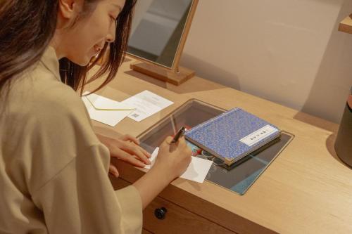a woman writing on a piece of paper on a desk at 메종 드 온유 호텔 전주 한옥마을점 in Jeonju