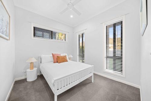 a white bedroom with a bed and two windows at Casa al mare - Bribie Island 5BD Retreat in Woorim