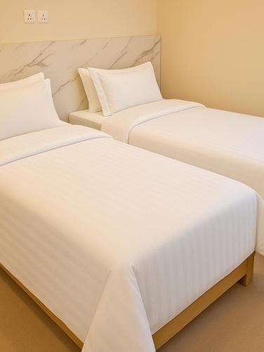 two beds in a room with white sheets at Scuba Haven Fuvahmulah in Fuvahmulah