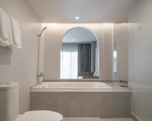 een badkamer met een badkuip, een toilet en een spiegel bij Terra Nara in Pattaya