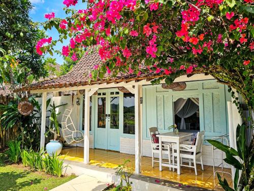 a cottage with a table and chairs on a deck with pink flowers at Janur Bungalow in Borobudur