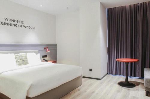 a bedroom with a bed and a stool and a table at City Comfort Premier Hotel Xiaogan Anlu Railway Station Dongda Times Square in Xiaogan