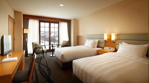 a hotel room with two beds and a desk at Lotte Arai Resort in Myoko