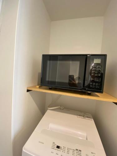 eine Mikrowelle auf einem Regal über einer Schachtel in der Unterkunft さくら旅館 吉祥寺千利休301号室 in Musashino