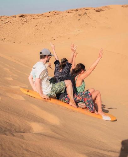 three people riding on a surfboard in the sand at Surf and Stay Villa Anza Taghazout Tamraght in Agadir