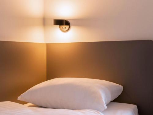 a bed with a white pillow and a light above it at B&B Hotel Weil am Rhein/Basel in Weil am Rhein