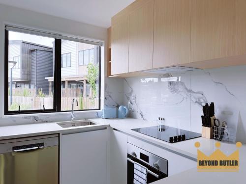 a white kitchen with a sink and a window at Discover Avondale - 10 Sec Walk to Sunday Market in Auckland