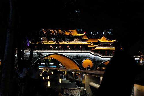 a bridge over a river with a city at night at BuYuan Hotel - Near Wuhou Shrine, Chunxi Road,T aikooli, Tianfu Square, People's Park, Chengdu Museum, Very close to the Sichuan University , Exit C of Huaxiba on Metro Line 1,Provides Welcome refreshments ,Minibar,Laundry & Luggage delivery service in Chengdu