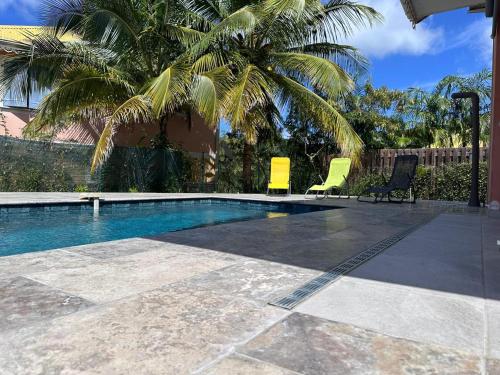 a swimming pool with two chairs and a palm tree at Villa Dézil in Les Anses-dʼArlets