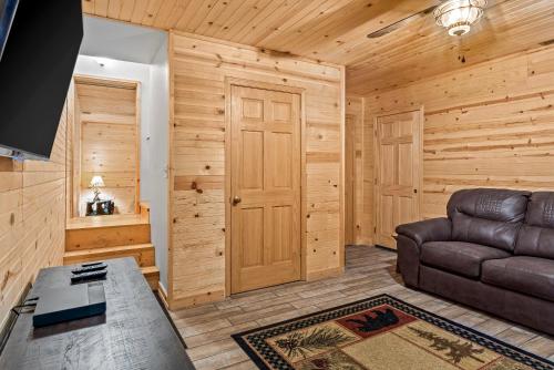a living room with a leather couch and wooden walls at The Cabin Kingdom Hot tub Fire Pit in Blairsville